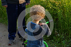 Adult man man scolds Little curly blonde boy with little bicycle