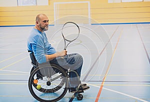 Adult man with a physical disability in a wheelchair playing tennis on indoor tennis court