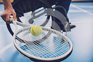 Adult man with a physical disability in a wheelchair playing tennis on indoor tennis court