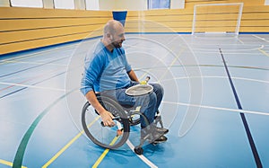 Adult man with a physical disability in a wheelchair playing tennis on indoor tennis court