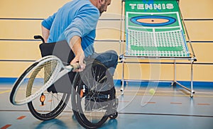 Adult man with a physical disability in a wheelchair playing tennis on indoor tennis court