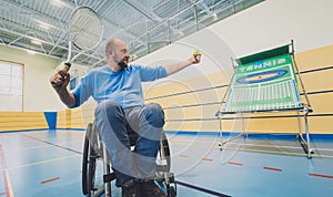 Adult man with a physical disability in a wheelchair playing tennis on indoor tennis court