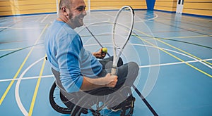 Adult man with a physical disability in a wheelchair playing tennis on indoor tennis court