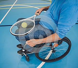 Adult man with a physical disability in a wheelchair playing tennis on indoor tennis court