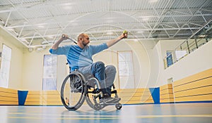 Adult man with a physical disability in a wheelchair playing tennis on indoor tennis court