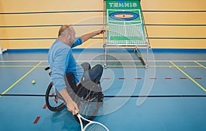 Adult man with a physical disability in a wheelchair playing tennis on indoor tennis court