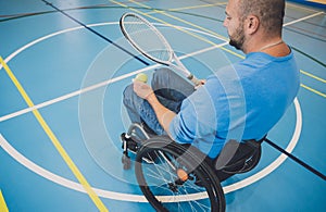 Adult man with a physical disability in a wheelchair playing tennis on indoor tennis court