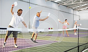 Adult man playing doubles pickleball with aged partner indoors