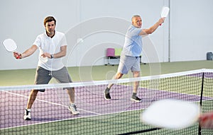 Adult man playing doubles pickleball in team with older partner