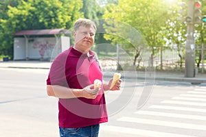 An adult man prone to fatness with two glasses of ice cream on a sunny day on a city street photo