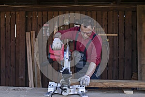 Adult man in protective overalls and glasses cuts wooden beam using circular saw