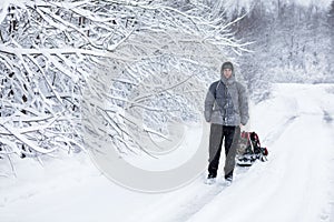 Adult man pulling sledge in the snow during strong snowfall