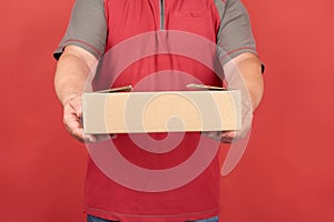Adult man in a red T-shirt holds a cardboard brown box on a red background