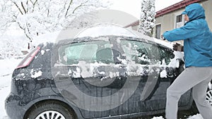 A adult man is removing snow from a car
