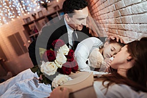 Adult man with roses bouquet is put to bed small daughter to sleep. Child is sleeping.