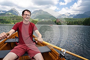 Adult man rowing boat on Strbske pleso Strba tarn in High Tatra mountains, Slovakia. Scenic landscape in background