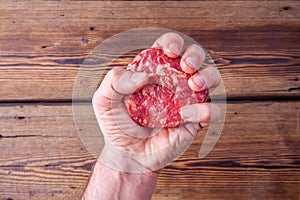 Adult man`s arm firmly holding a raw beef burger meat on a wooden background