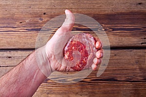 Adult man`s hand holding a raw beef burger meat showing thumb up like symbol