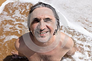 Adult man sitting on yellow sand in a foam wave, Greece, Crete, Chania