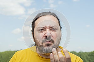 An adult man with a small beard demonstrates his severe irritation with a gesture