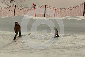 An adult man, standing on skis, teaches a small child to ski