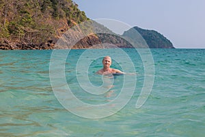 An adult man swims in the sea against the backdrop of mountains in Thailand, on the island of Koh Chang. Summer vacation at sea,