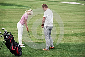 Adult man teaching the woman how to play the golf on the field with green grass