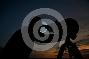 Adult man using a telescope at sunset time observing the moon at night. Amateur astronomy concept with empty copy space