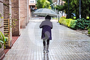 An adult man walked down the street of a city with a black umbrella on a rainy day