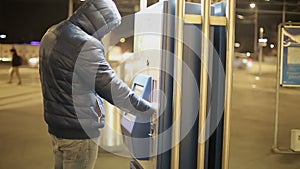 An adult man in a warm jacket uses the touch screen of the parking machine to pay for car parking.