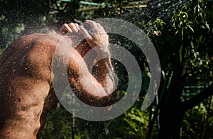 Adult man is washing himself under the summer shower in the garden