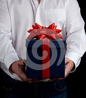 Adult man in a white shirt holds a blue gift cardboard box with a red bow