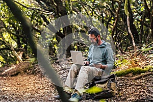 Adult man work with computer laptop and roaming phone connection in the middle of the green wild forest - concept of digital nomad