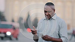 Adult mature black man holding smartphone looking at phone screen look for address with electronic map in city. Elderly