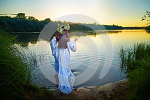 Adult mature brunette woman in a white dress, sundress and a wreath of flowers in summer in water of river or lake in