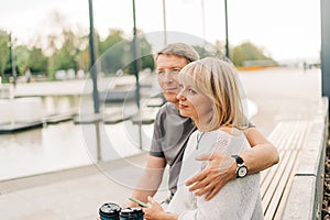 An adult mature happy couple in love sitting on bench outdoors in city street park. A blonde caucasian man and woman