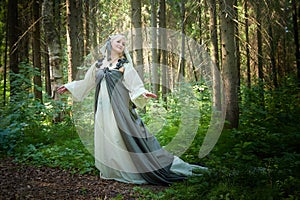 Adult mature woman 40-60 in a green long fairy dress in forest. Photo shoot in style of dryad and queen of nature. Fairy