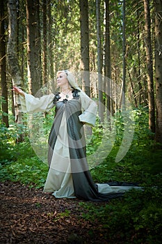 Adult mature woman 40-60 in a green long fairy dress in forest. Photo shoot in style of dryad and queen of nature. Fairy