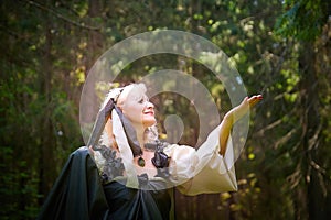 Adult mature woman 40-60 in a green long fairy dress in forest. Photo shoot in style of dryad and queen of nature. Fairy