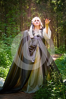 Adult mature woman 40-60 in a green long fairy dress in forest. Photo shoot in style of dryad and queen of nature. Fairy