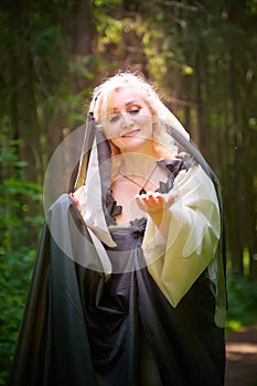 Adult mature woman 40-60 in a green long fairy dress in forest. Photo shoot in style of dryad and queen of nature. Fairy