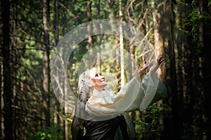 Adult mature woman 40-60 in a green long fairy dress in forest. Photo shoot in style of dryad and queen of nature. Fairy