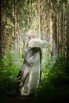 Adult mature woman 40-60 in a green long fairy dress in forest. Photo shoot in style of dryad and queen of nature. Fairy