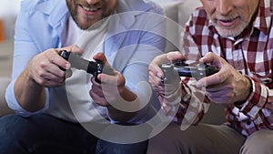 Adult men playing video games using game joysticks, father and son having fun