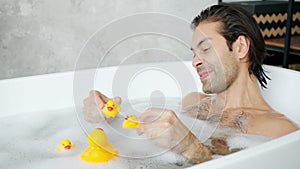 Adult mixed race guy having with toys playing with rubber ducks in bathtub