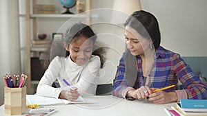 Adult mixed race woman teacher sitting and talking to american black student child in school class during day.