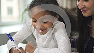 Adult mixed race woman teacher sitting and talking to american black student child in school class during day.