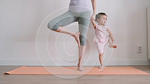Adult mom with her pretty little baby practising yoga on a mat at home