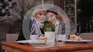 Adult mother and daughter in cafe in autumn, they drink coffee and cakes.