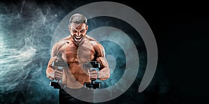 Adult muscular man screaming while working out hard with dumbbells on dark studio background with smoke